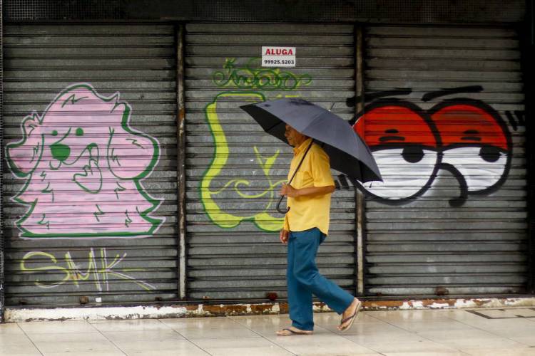 Homem em primeiro plano com guarda-chuva, passando em portão com grafites. Praia de Iracema, Fortaleza.