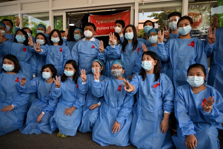 Uma equipe médica faz uma saudação de três dedos com uma fita vermelha em um uniforme no Hospital Geral de Yangon em Yangon em 3 de fevereiro de 2021, enquanto os apelos por uma desobediência civil ganham força após um golpe militar que deteve a líder civil Aung San Suu Kyi. 