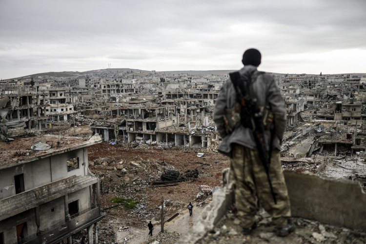 ￼Atirador curdo está no topo de um prédio enquanto olha para a aldeia destruída de Halimce, a leste da cidade síria de Kobane