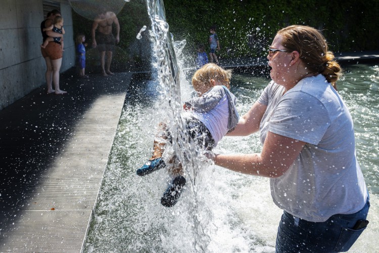 Uma mulher segura uma criança sob uma cachoeira em um parque em Washington, DC, em 2021, durante uma onda de calor nos Estados Unidos