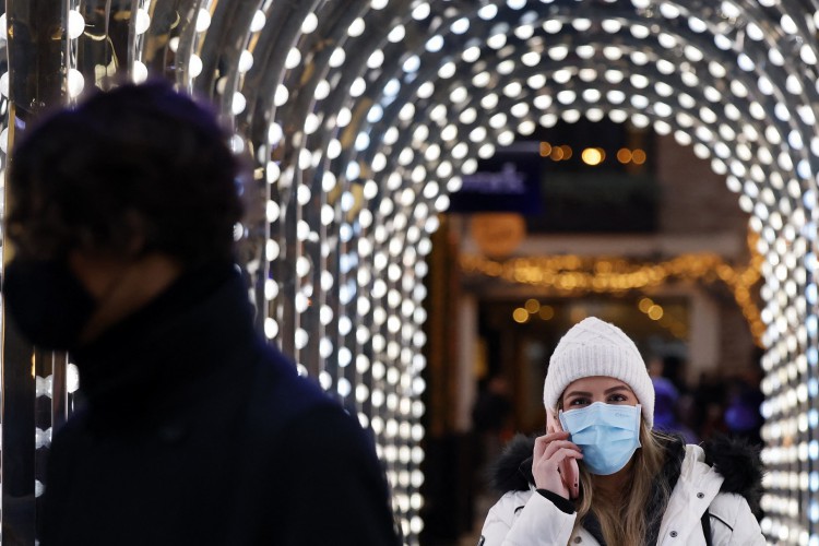 Pedestres, alguns usando coberturas faciais para combater a propagação de Covid-19, caminham por um arco coberto de luz perto de lojas no último sábado para fazer compras antes do Natal, no centro de Londres em 18 de dezembro de 2021