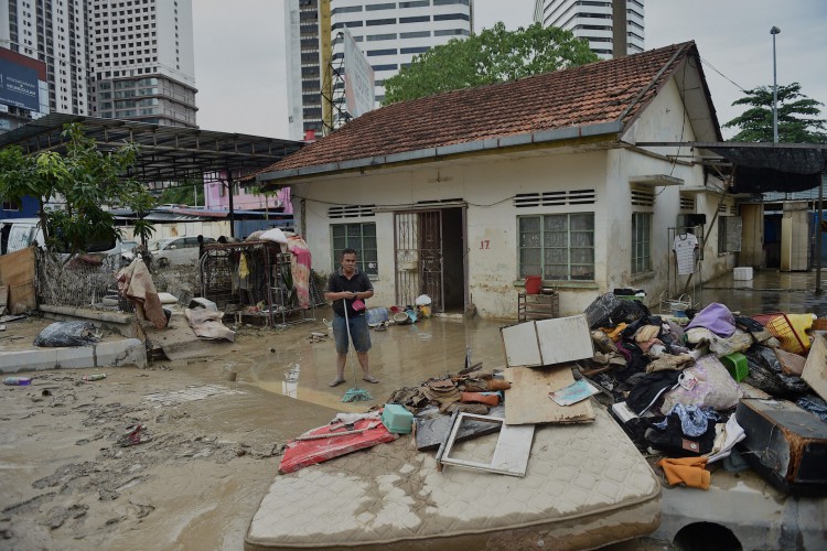 Um homem limpa lama de sua casa depois que ela foi atingida por uma enchente em Kuala Lumpur, Malásia