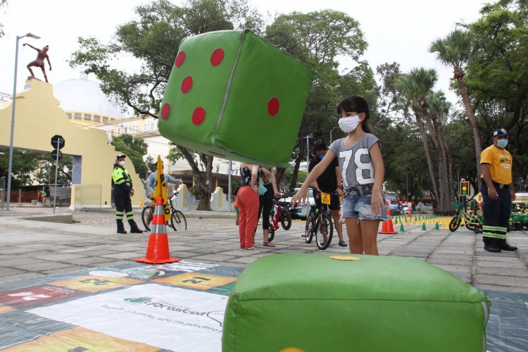 Crianças brincam em jogo de tabuleiro gigante com instruções educativas sobre o trânsito. A prefeitura de Fortaleza, por meio da AMC, promove a primeira edição do projeto Minicircuito de Bike Infantil