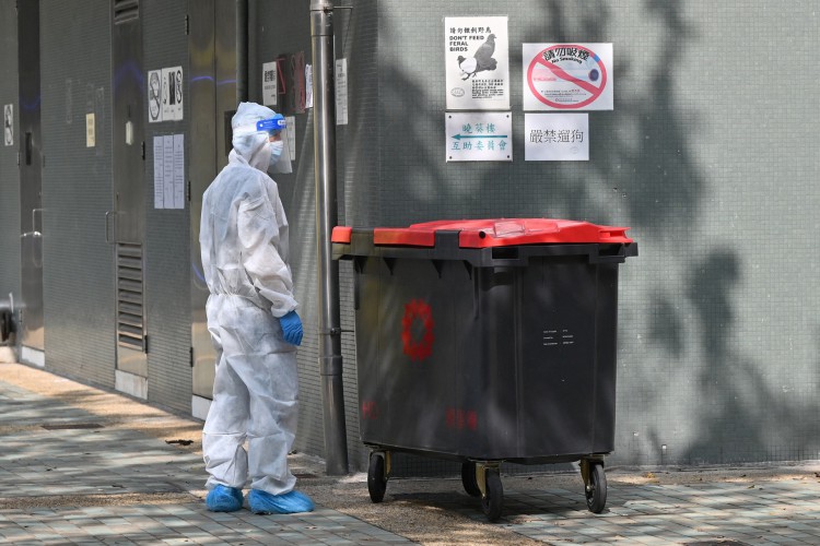 Um trabalhador com roupas de proteção completas para se proteger contra o Covid-19 esvazia uma lixeira no conjunto habitacional de Kwai Chung, em Hong Kong