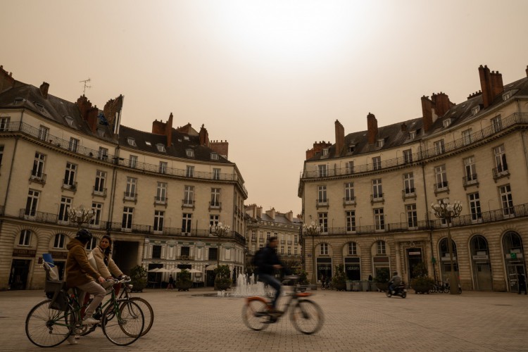 Moradores andam de bicicleta na praça Graslin sob um céu amarelo ocre causado pela poeira do Saara em Nantes, oeste da França, em 15 de março de 2022.
