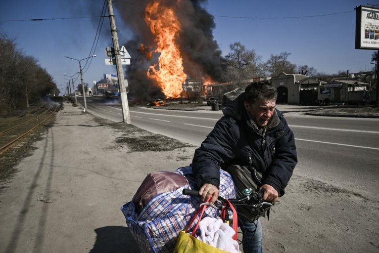 Um homem foge com seus pertences enquanto o fogo envolve um veículo e um prédio após fogo de artilharia no 30º dia da invasão da Ucrânia por forças russas na cidade de Kharkiv, no nordeste, em 25 de março de 2022. cidade de Kharkiv em 25 de março de 2022, matando pelo menos quatro civis e ferindo vários outros, disseram autoridades ucranianas