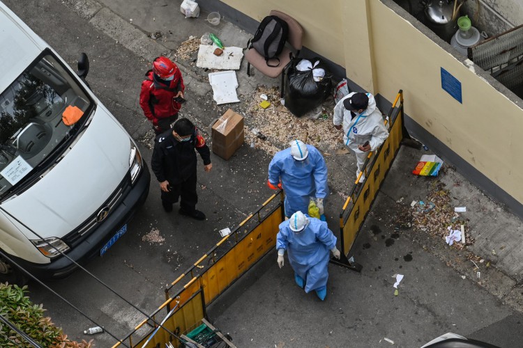 Profissionais de saúde usando equipamentos de proteção individual (EPI) atravessam um posto de controle durante um bloqueio de coronavírus Covid-19 no distrito de Jing'an, em Xangai, em 16 de abril de 2022.