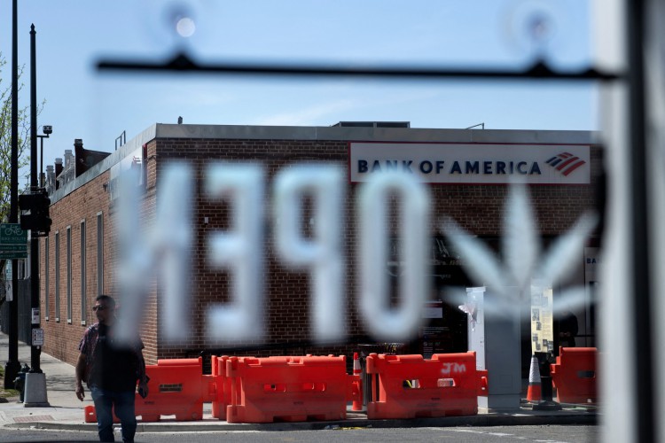 Homem caminha perto de um Bank of America enquanto uma folha de maconha é vista na placa aberta na loja de cannabis Sneaker Headz em 15 de abril de 2022, em Washington,