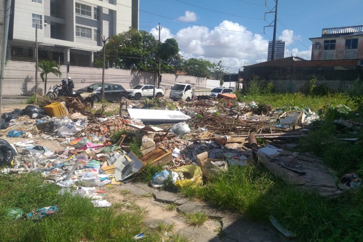 Pedestres têm dificuldade de caminhar na calçada da rua Érico Mota, tomada por lixo na altura do terreno abandonado 