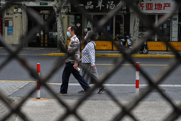 Pessoas caminham em uma rua vista através da cerca de um complexo fechado durante um bloqueio de coronavírus Covid-19 no distrito de Jing'an, em Xangai, em 19 de maio de 2022