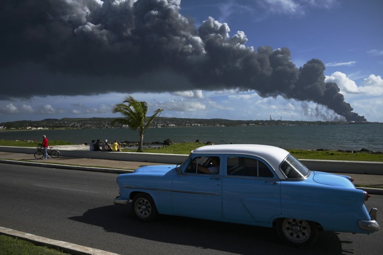 Fumaça preta de um tanque de óleo em chamas é vista enquanto um velho carro americano passa por uma rua em Matanzas, Cuba, em 6 de agosto de 2022. O incêndio causado por um raio na sexta-feira em um depósito de combustível em Matanzas, no oeste de Cuba, se espalhou para um segundo tanque na madrugada deste sábado e causou 49 feridos, informaram fontes oficiais.