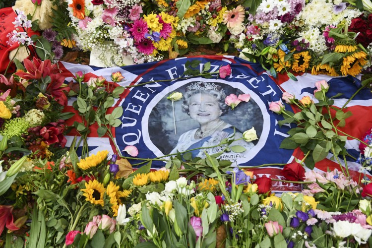 Uma bandeira com a foto da rainha Elizabeth II da Grã-Bretanha é vista entre flores colocadas por simpatizantes perto do Palácio de Buckingham, em Londres, em 11 de setembro de 2022