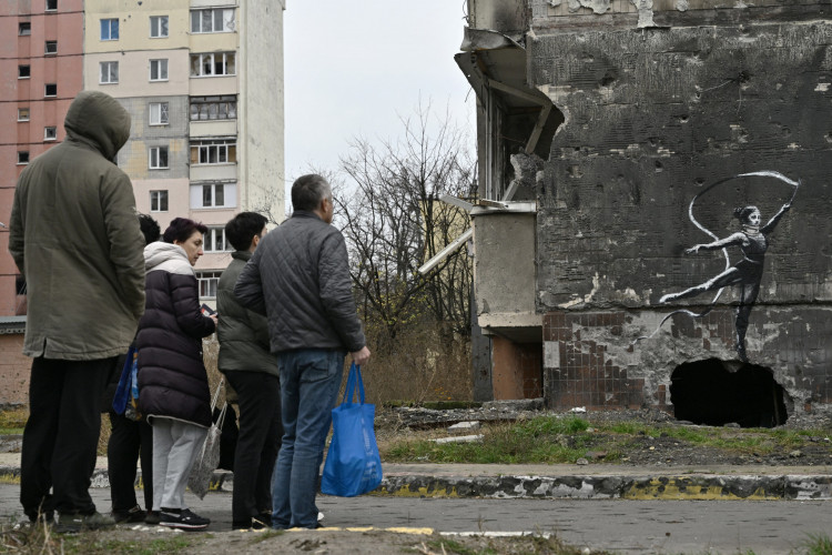 Moradores conferem mural pintado no estilo do artista Banksy em muro de prédio destruído nos arredores de Kiev, na Ucrânia