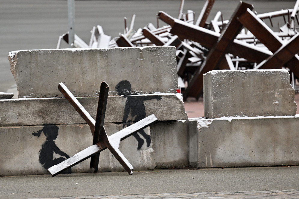 Esta fotografia tirada em 17 de novembro de 2022 mostra uma peça do artista de rua britânico Banksy em construções antitanque cobertas de neve, após as primeiras nevascas da temporada, na Praça da Independência em Kyiv, em meio à invasão russa da Ucrânia. (Foto: Sergei SUPINSKY / AFP)