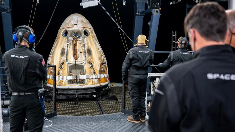 Neste folheto da NASA, as equipes de suporte fotográfico a bordo da nave de recuperação da SpaceX, Shannon, trabalham em torno da espaçonave SpaceX