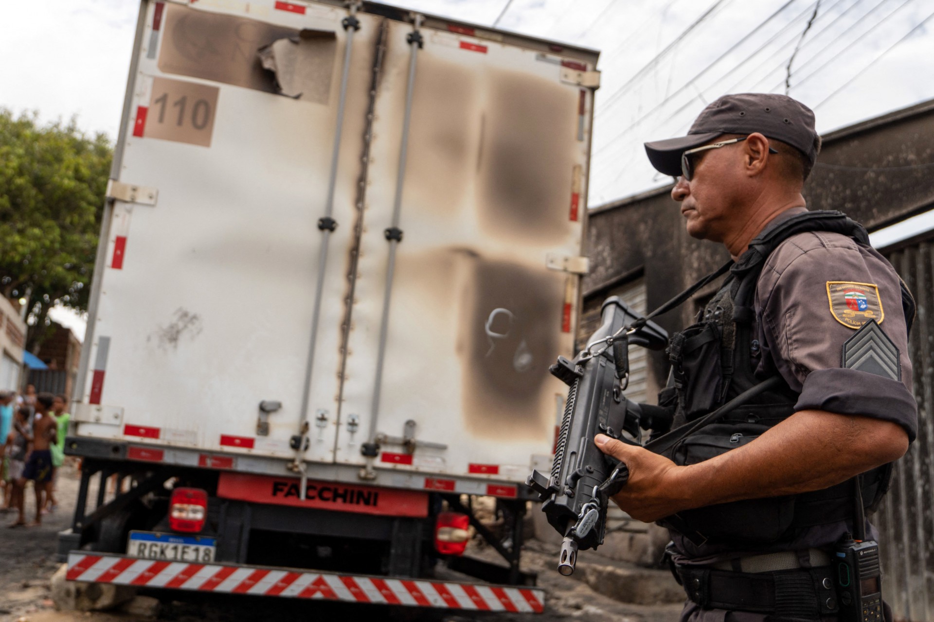 Um policial fica de guarda ao lado de um caminhão comercial queimado em Natal, estado do Rio Grande do Norte, Brasil, em 16 de março de 2023. Membros de gangues incendiaram carros, atiraram em prédios públicos e semearam terror na quarta-feira em uma onda de ataques antes do amanhecer em várias cidades do nordeste do Brasil que já dura duas noites, disseram as autoridades. Autoridades disseram que os ataques no estado do Rio Grande do Norte, que começaram na noite de segunda-feira, foram planejados de dentro da prisão por líderes de gangues como um protesto contra as condições das prisões e retaliação às novas regras que reprimem as operações das facções criminosas dentro do sistema penal. (Foto: Alessandro IMPERIAL/AFP)