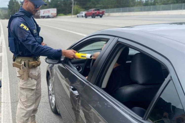 Policial da PRF realiza o teste do bafômetro em um motorista. 