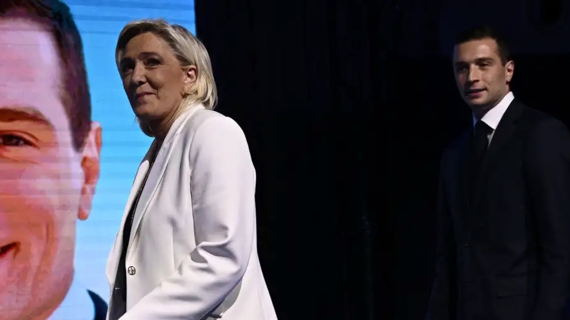 Marine Le Pen, do partido ultradireitista francês Reunião Nacional, diante de telão com o rosto do presidente da sigla e candidato a primeiro-ministro Jordan Bardella (Foto: Julien de Rosa/AFP)