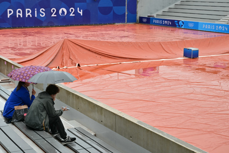 Os espectadores se protegem da chuva enquanto o tempo chuvoso atrasa o início dos jogos nas quadras externas do Estádio Roland-Garros dos Jogos Olímpicos de Paris 2024, no sábado, 27