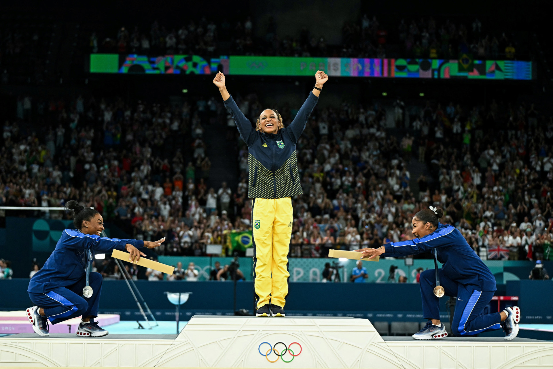 Rebeca Andrade é reverenciada pelas ginastas dos EUA Simone Biles (prata) e Jordan Chiles (bronze) ao receber medalha de ouro nas Olimpíadas 2024, em Paris  (Foto: GABRIEL BOUYS / AFP)