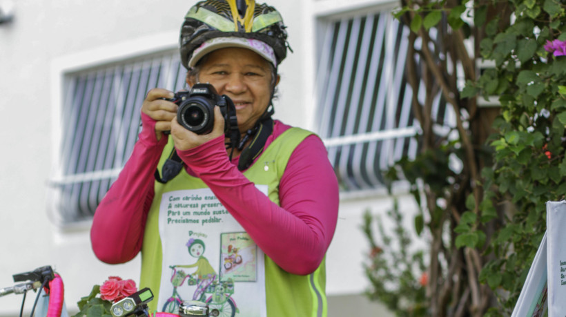 Maria Rosa Rodrigues, ciclista, fotógrafa e escritora. Rosa posa com sua câmera fotografia, também companheira de pedalada. 