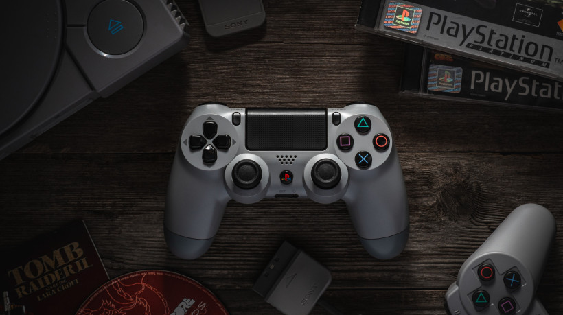 Odessa, Ukraine - December 7, 2019: The DualShock4 Wireless Controller for PlayStation4. Gamepad gray for PS4 on a vintage wooden table among the PS1 console and games for it. 