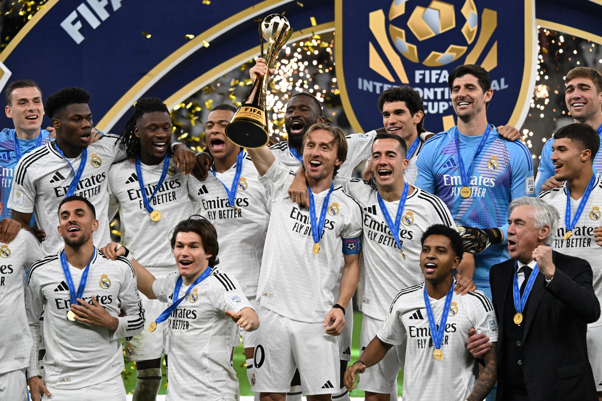 O meio-campista croata #10 do Real Madrid, Luka Modric, comemora com o troféu do torneio enquanto posa com seus companheiros de equipe e treinador para a foto do grupo na cerimônia do pódio após a partida de futebol final da Copa Intercontinental da FIFA de 2024 entre o Real Madrid da Espanha e o Pachuca do México no Estádio Lusail em Doha em 18 de dezembro de 2024 (Foto: Mahmud HAMS / AFP)