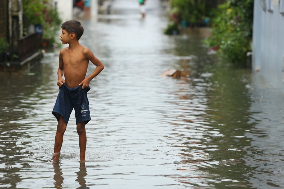 Imagem da chuva em Fortaleza. Menino enfrenta as águas em rua alagada vestindo apenas um shorts de fardamento escolar(Foto: FÁBIO LIMA)