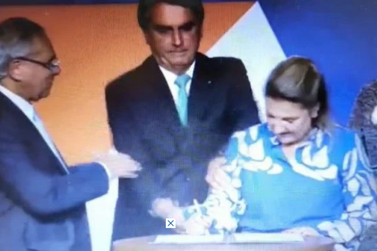 Presidente Jair Bolsonaro (PL) aperta o braço da nova presidente da Caixa Econômica Federal, Daniella Marques, para retirar uma caneta de suas mãos