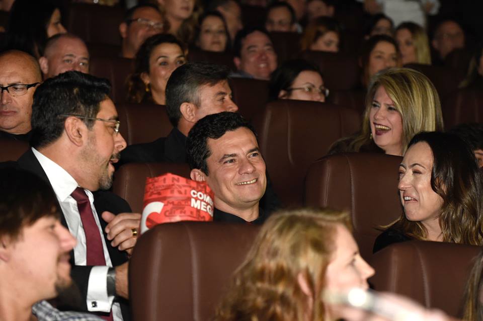 Sérgio Moro aparece no centro da imagem, ao lado da mulher, Rosângela e do colega Marcelo Bretas. Todos estão no cinema assistindo à primeira exibição do longa-metragem sobre a operação Lava Jato